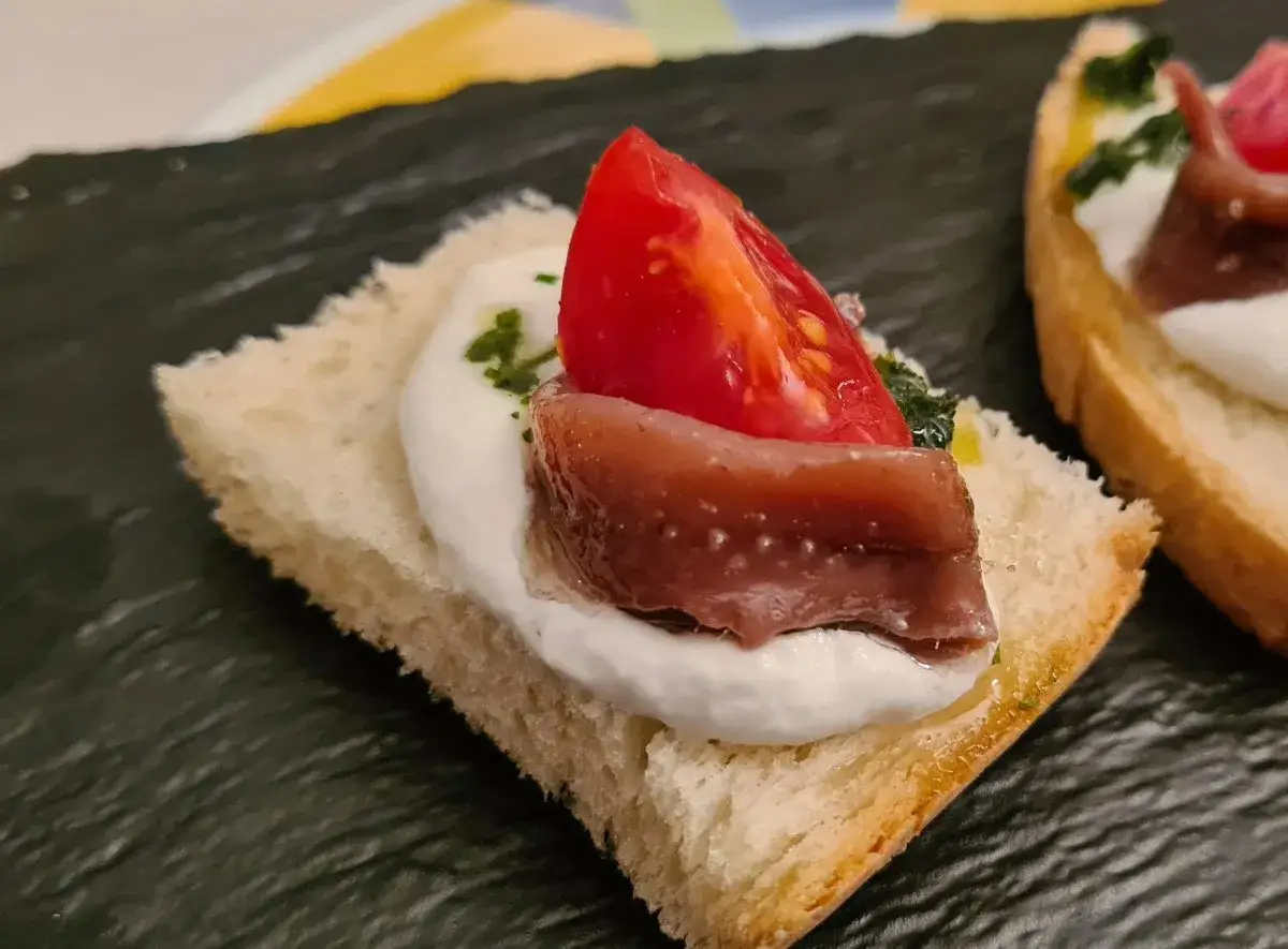 Deliziosi crostini con burrata cremosa, pomodoro fresco e alici del Cantabrico, un antipasto che sa di mare e di sole.