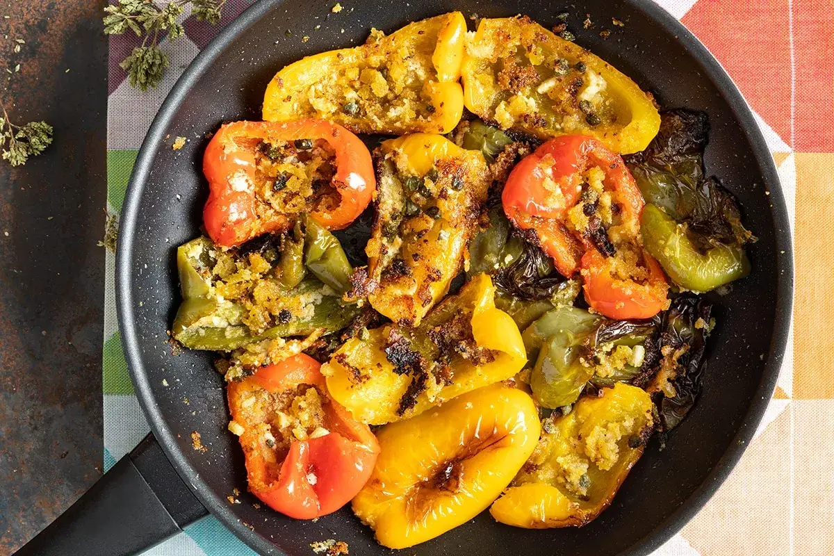 Peperoni ammollicati cotti in padella, ripieni di pangrattato e erbe aromatiche, con colori vivaci e dorati.