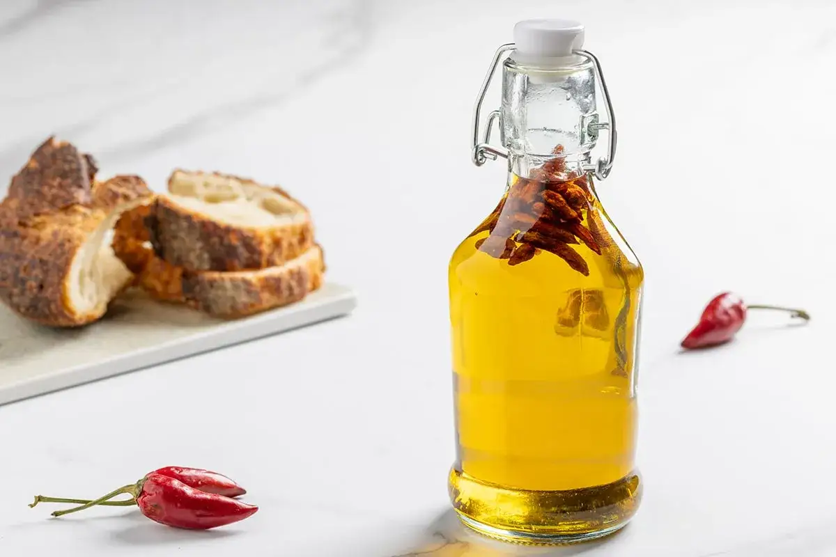 Olio al peperoncino in bottiglia, con peperoncini rossi e pane rustico a fette.