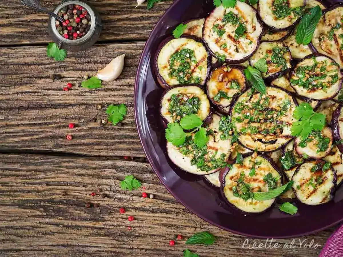 Fette di melanzane grigliate condite con erbe fresche e aglio, un contorno saporito e colorato.