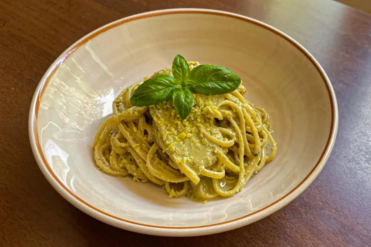 Spaghetti conditi con un cremoso pesto di limone, guarniti con basilico fresco. Una deliziosa ricetta per un primo piatto estivo.