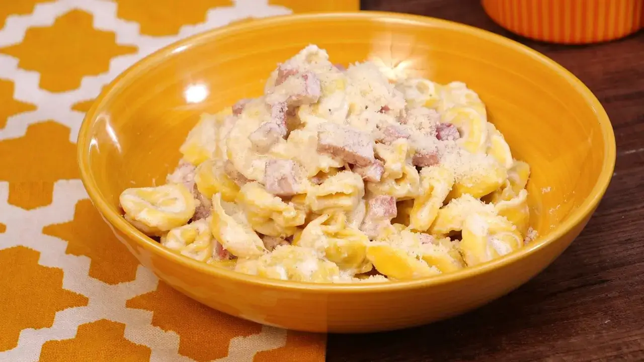 Tortellini panna e prosciutto, un piatto cremoso e saporito, servito in una ciotola gialla con parmigiano grattugiato.