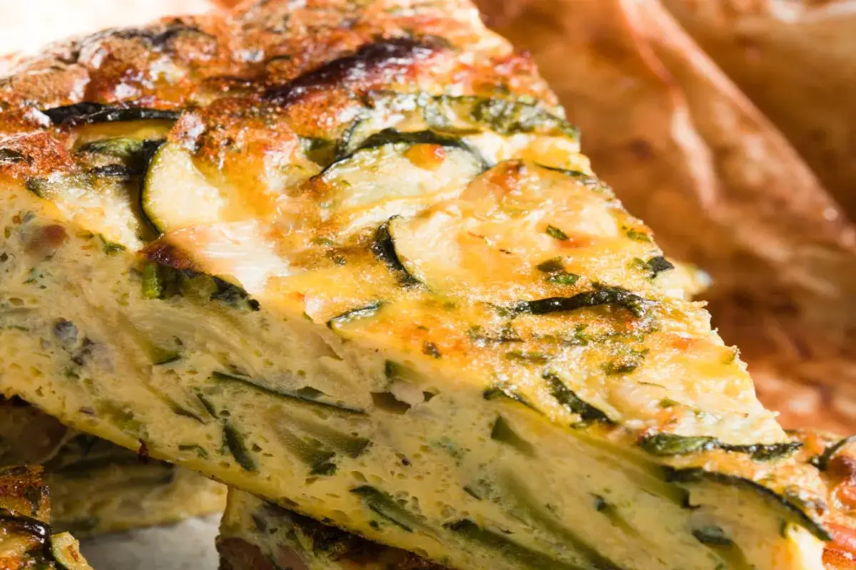 Una fetta di torta salata con zucchine, dorata e invitante, con verdure fresche e formaggio filante.