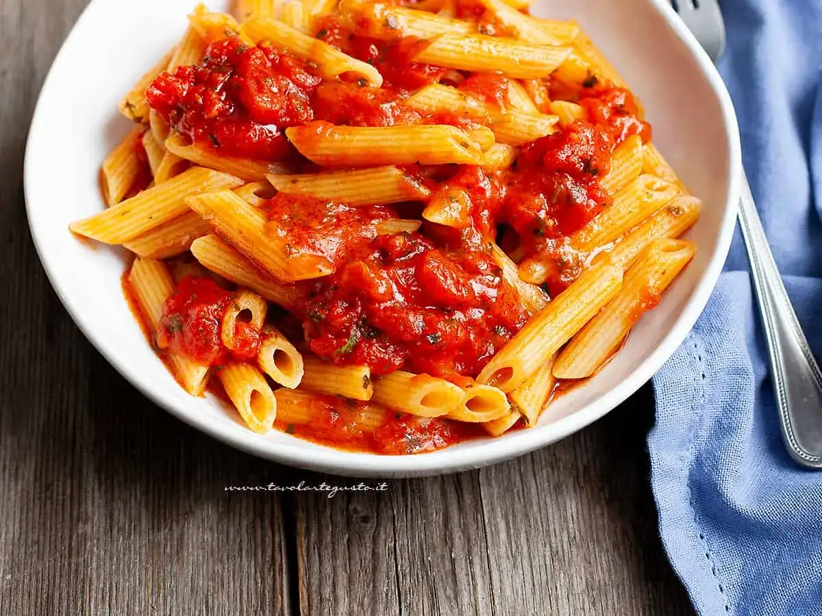 Piatto fumante di penne all'arrabbiata, con sugo rosso piccante e basilico fresco.