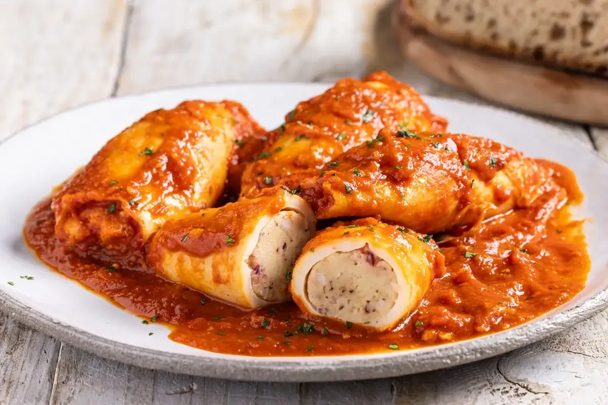 Deliziosi calamari ripieni in padella, cotti in un ricco sugo di pomodoro e guarniti con prezzemolo fresco.