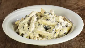 Penne cremose con pezzetti scuri, un piatto invitante di pasta alla cenere, servito in una ciotola bianca su un tavolo di legno rustico.