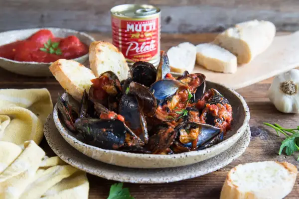 Piatto fumante di cozze alla tarantina ricetta, con pane tostato e pomodori pelati Mutti.