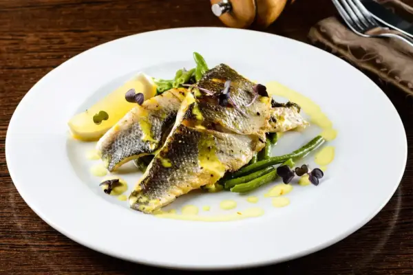 Deliziosi secondi di pesce con fagiolini croccanti, limone e una salsa gialla cremosa, guarniti con erbe viola.