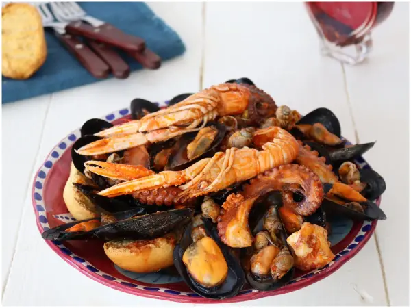Un piatto ricco di zuppa di cozze, scampi e polpo, servito con pane tostato.
