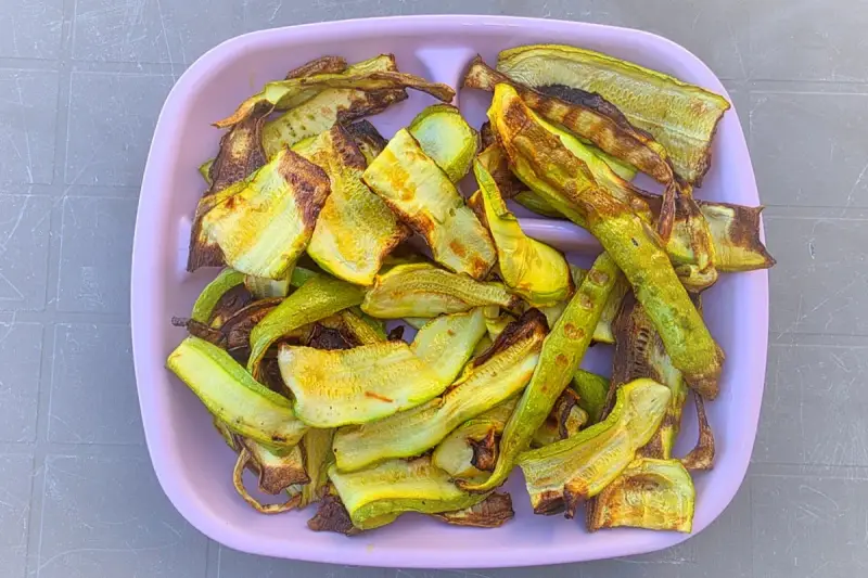 Piatto rosa pieno di zucchine grigliate, tagliate a listarelle e leggermente abbrustolite, pronte per essere gustate.