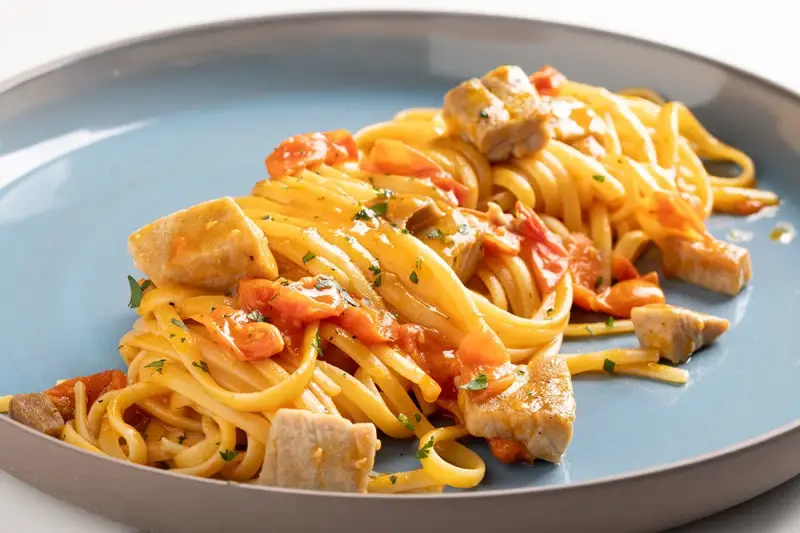 Un piatto invitante di pasta con tonno fresco, pomodorini e prezzemolo, condito con una salsa dorata.