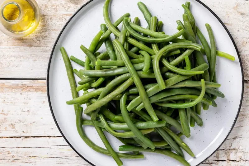 Un piatto di fagiolini lessi, freschi e verdi, pronti per essere gustati. Accanto, un piccolo recipiente con olio d'oliva.
